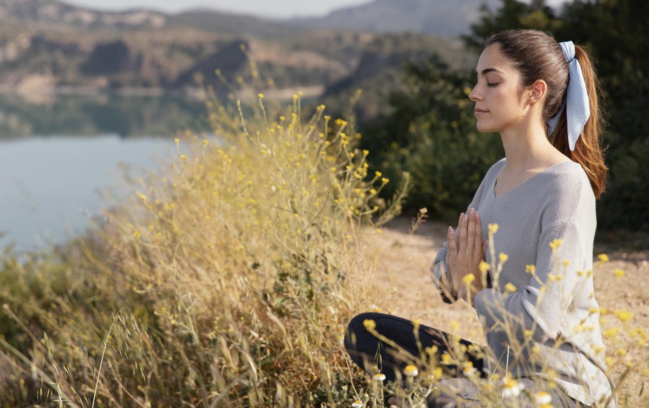 Relaxed woman meditating outdoors surrounded by nature for stress relief and emotional balance
